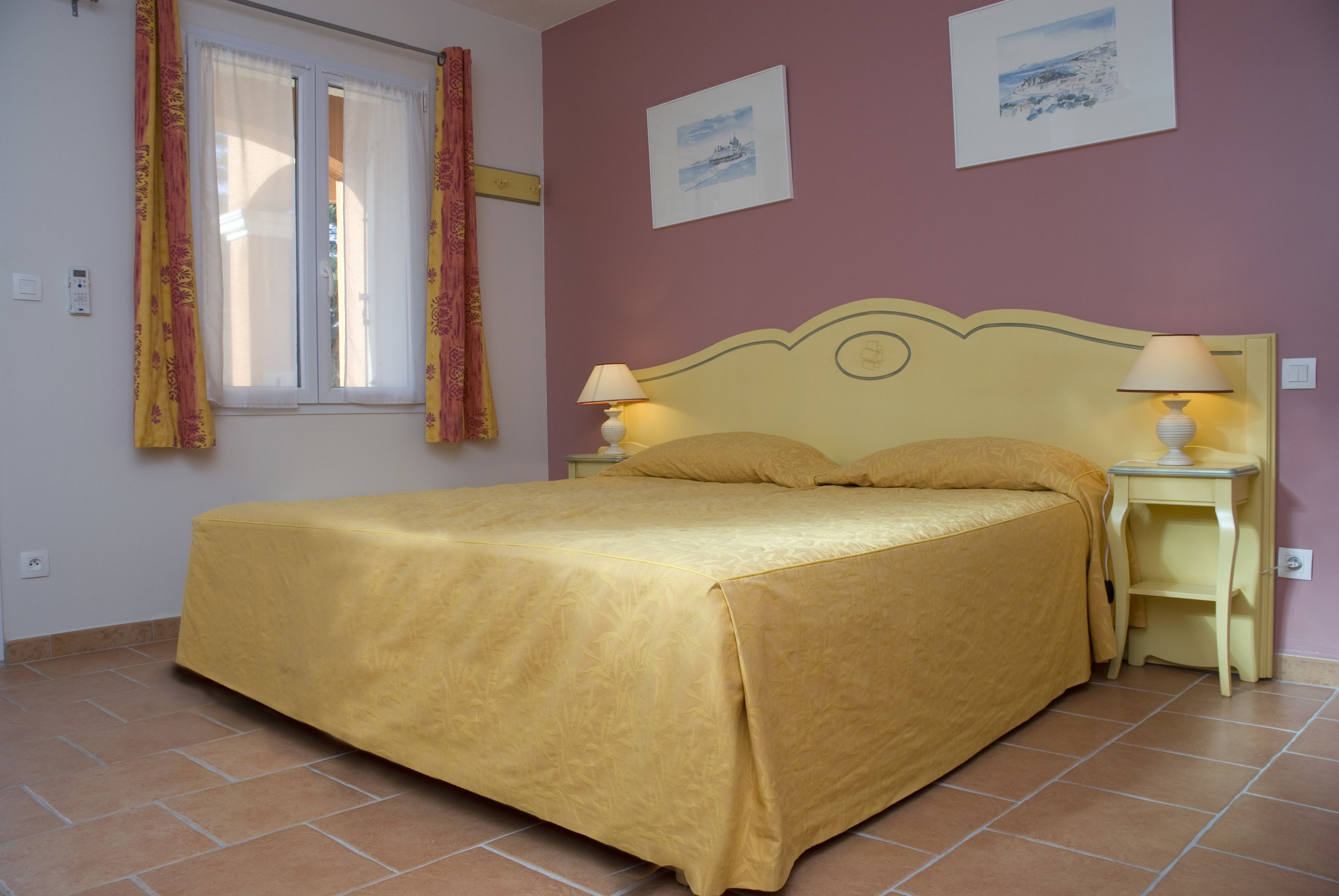 Une chambre à coucher avec un lit, deux tables de chevet avec des lampes, une fenêtre avec des rideaux et deux tableaux encadrés accrochés au mur.