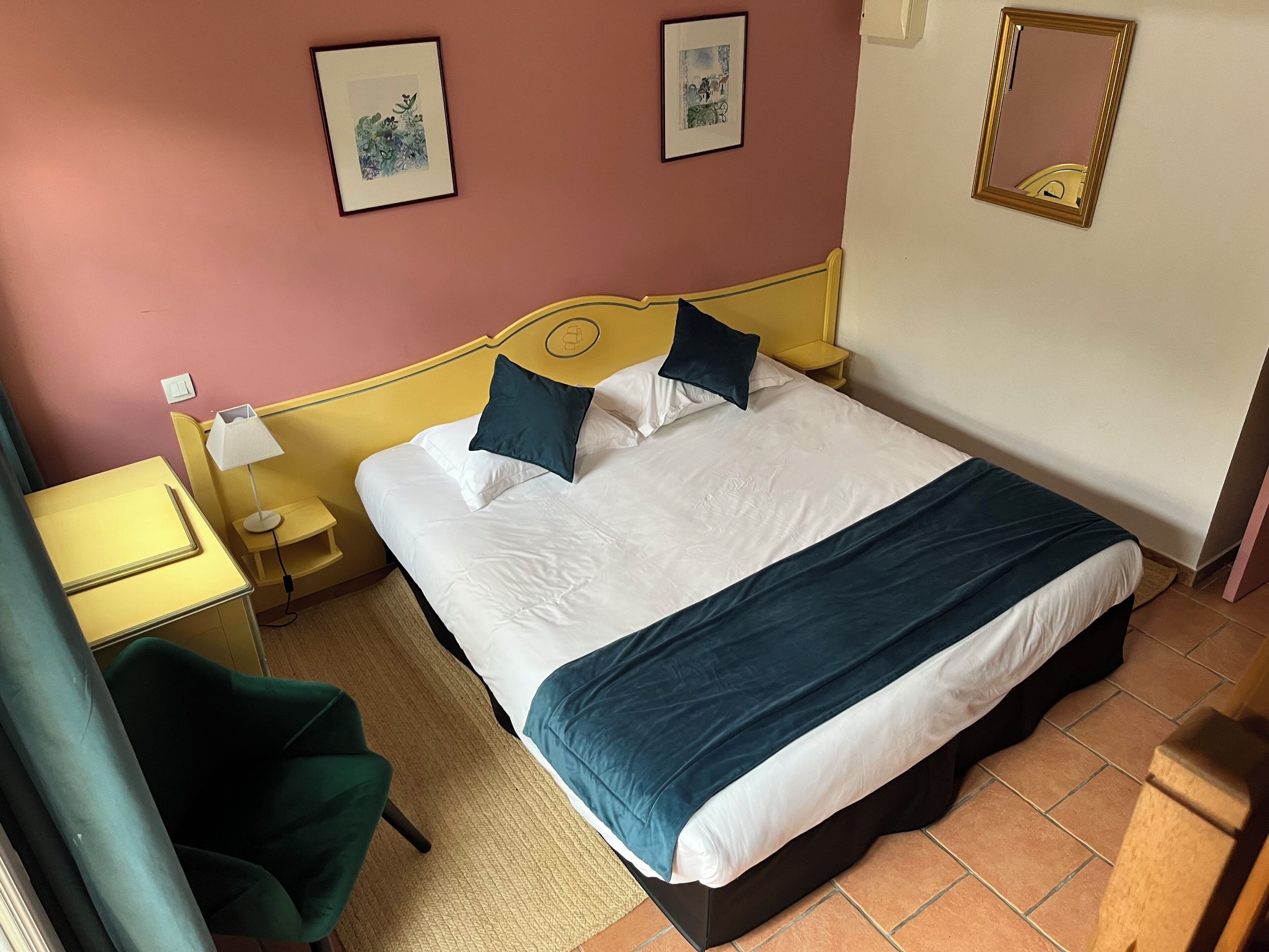 Ein Hotelzimmer mit Bett, Nachttischen, Schreibtisch, Stuhl und zwei gerahmten Bildern an der Wand.