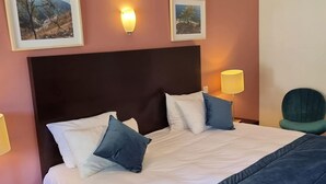 A neatly made bed with white and blue pillows, a dark headboard, and framed pictures on the wall.