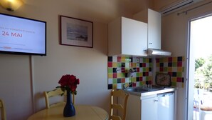 A small kitchen with a sink, a stove, and a window. There is a table with chairs and a vase of flowers.