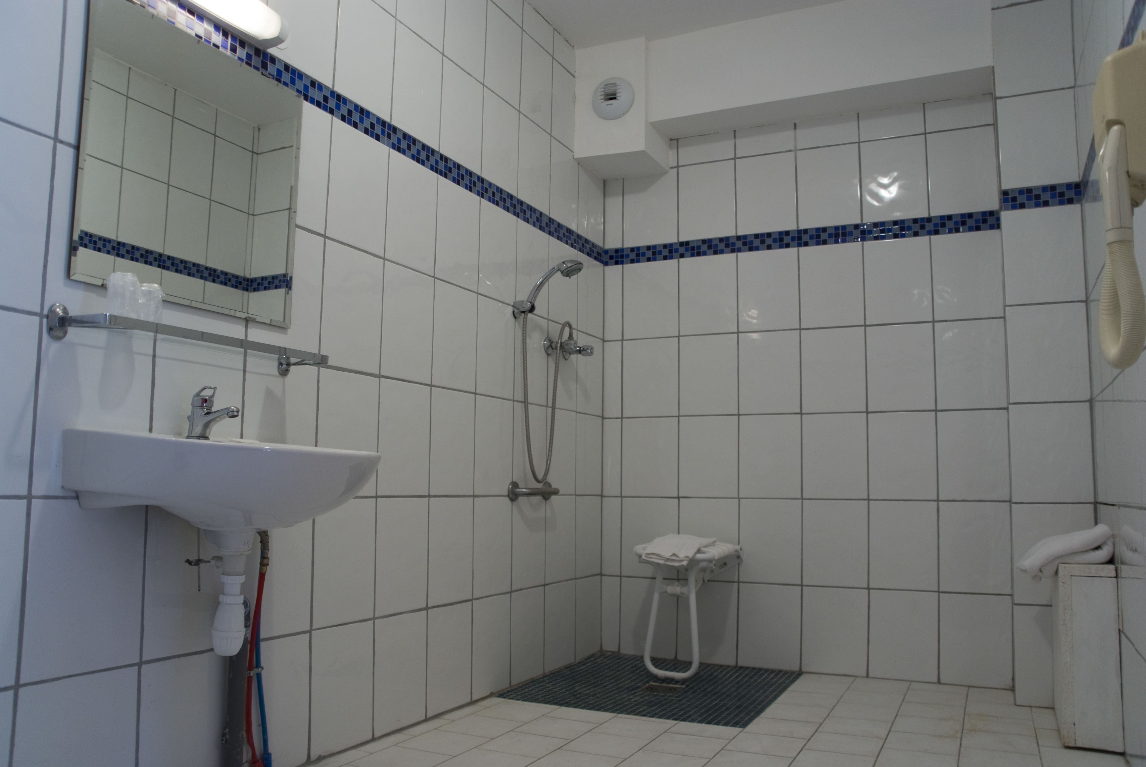 A small, tiled bathroom with a sink, mirror, shower, and toilet.