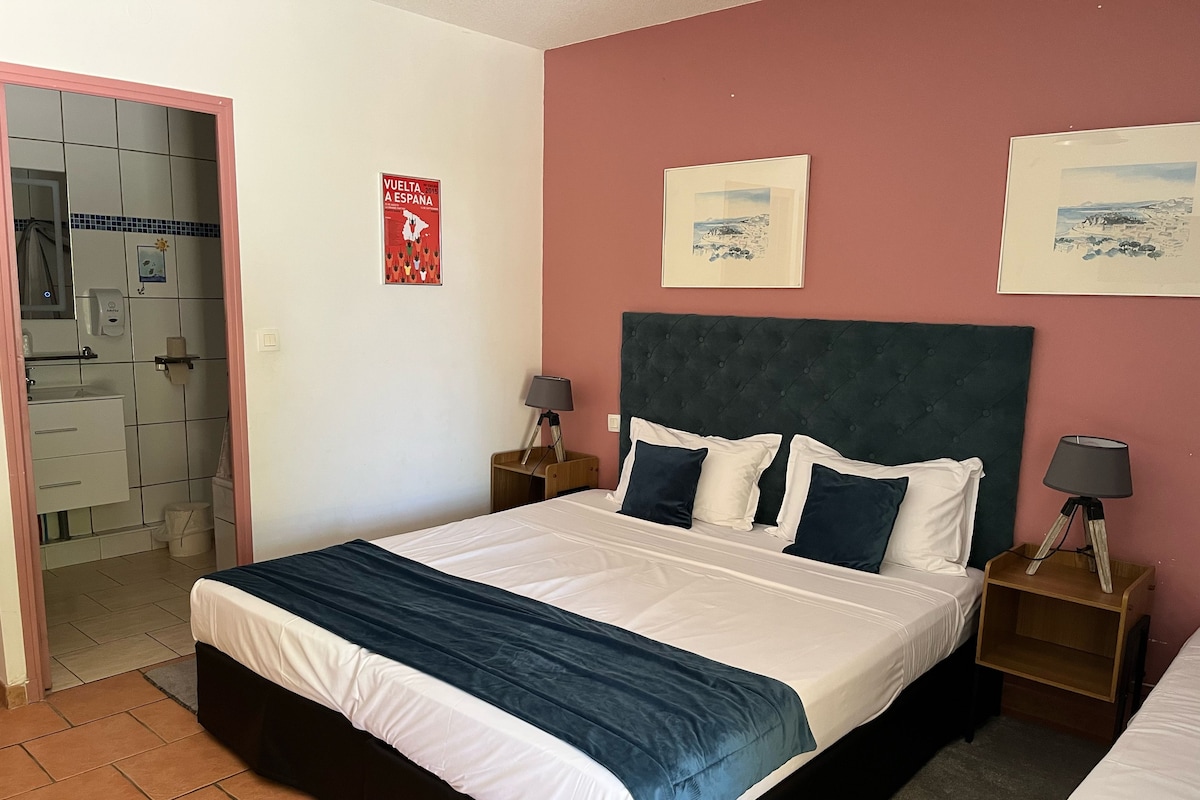 Een slaapkamer met een bed, twee nachtkastjes, een poster aan de muur, en een badkamer zichtbaar door een open deur.