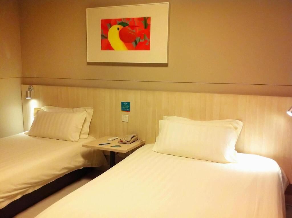 Une chambre d’hôtel avec deux lits, une table de chevet, un téléphone et un tableau encadré au mur.