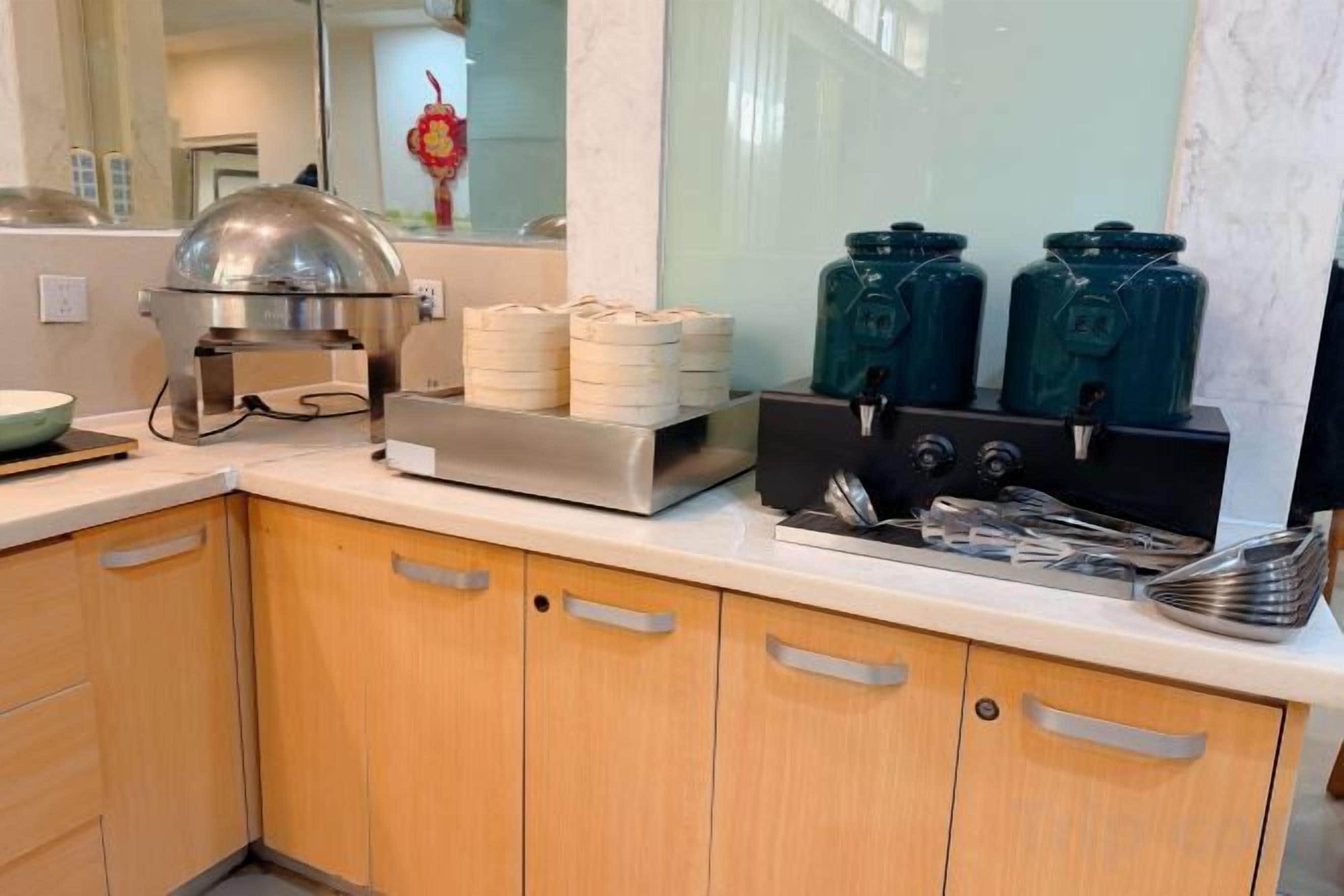 A kitchen with a buffet setup including a food warming station, stacked plates, and condiment dispensers.