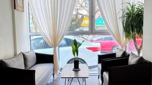 A hotel room with a sofa, a small table, and a view of the street through large windows.
