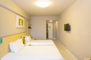 A hotel room with two beds, a flat-screen TV mounted on the wall, and a hallway leading to another room.