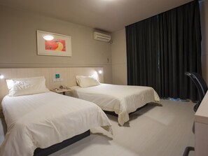 Ein Hotelzimmer mit zwei Betten, einem Schreibtisch, einem Telefon, einer Klimaanlage und einem Fenster mit Vorhängen.
