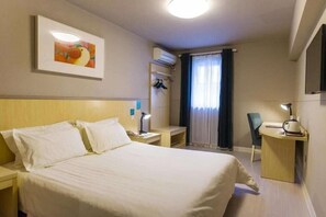 Ein Hotelzimmer mit Bett, Nachttischen, Schreibtisch, Stuhl, Klimaanlage und einem Fenster mit Vorhängen.