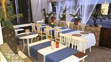 An outdoor dining area with tables and chairs, potted plants, and a view of the street.