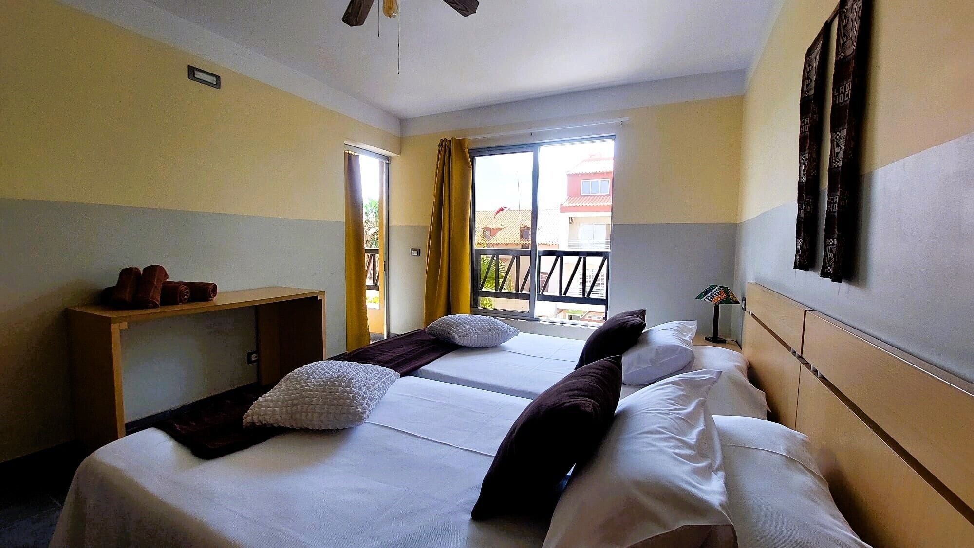 A hotel room with two beds, a desk, and a window with a view of buildings outside.