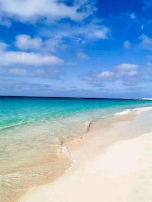 Een strand met helder turquoise water en een zandkust onder een licht bewolkte lucht.