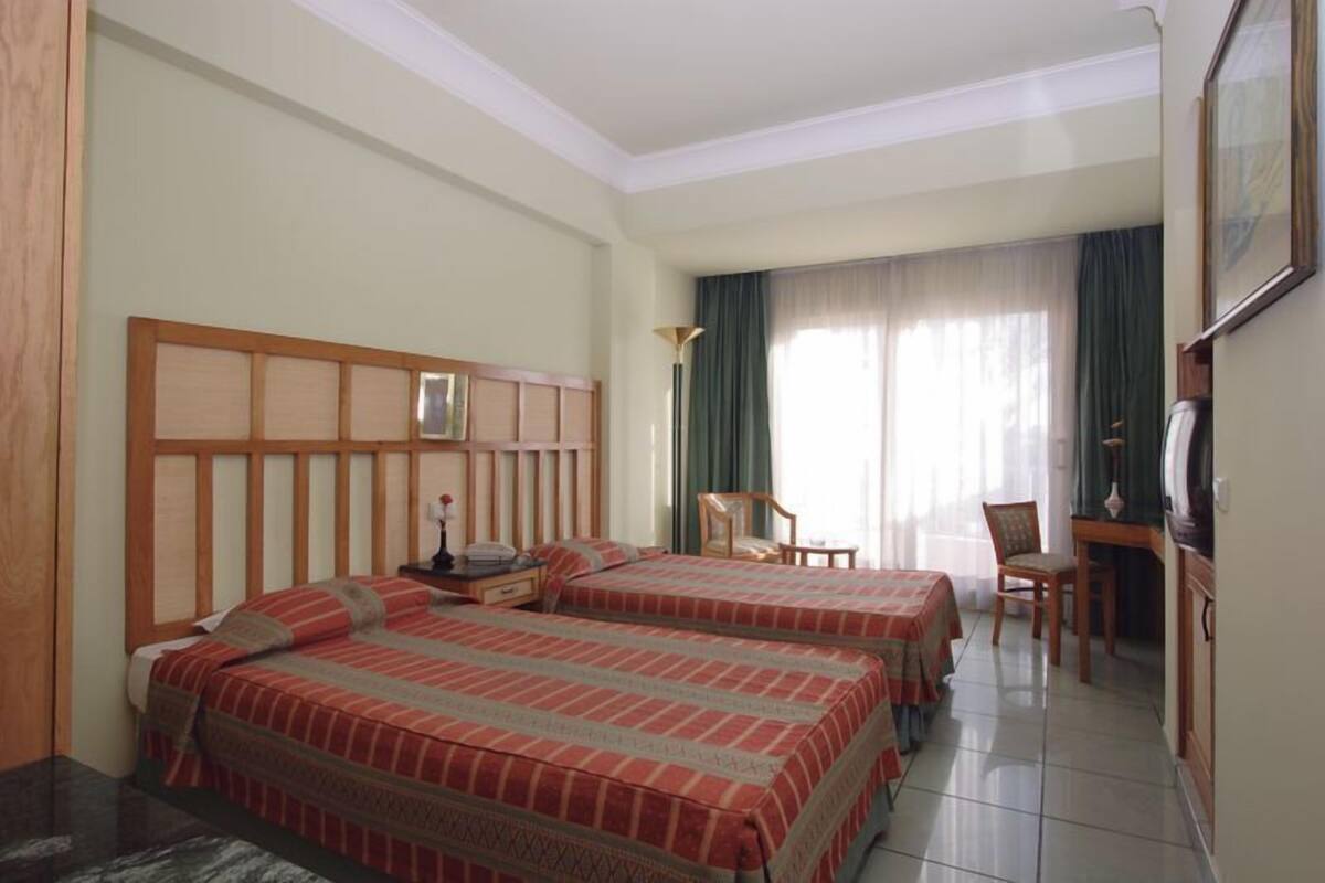 A hotel room with two beds, a desk, a chair, and a television.