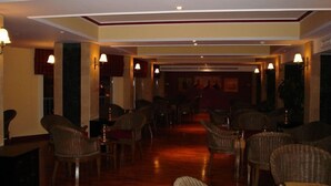 Un'accogliente hall d'albergo con poltrone in vimini disposte in file, pavimento in legno e lampade a parete.