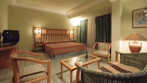 Una camera d'albergo con un letto, due poltrone, un tavolo, una televisione e una lampada.