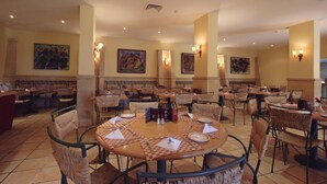 Un'ampia sala da pranzo con tavoli rotondi, sedie in vimini e opere d'arte alle pareti.