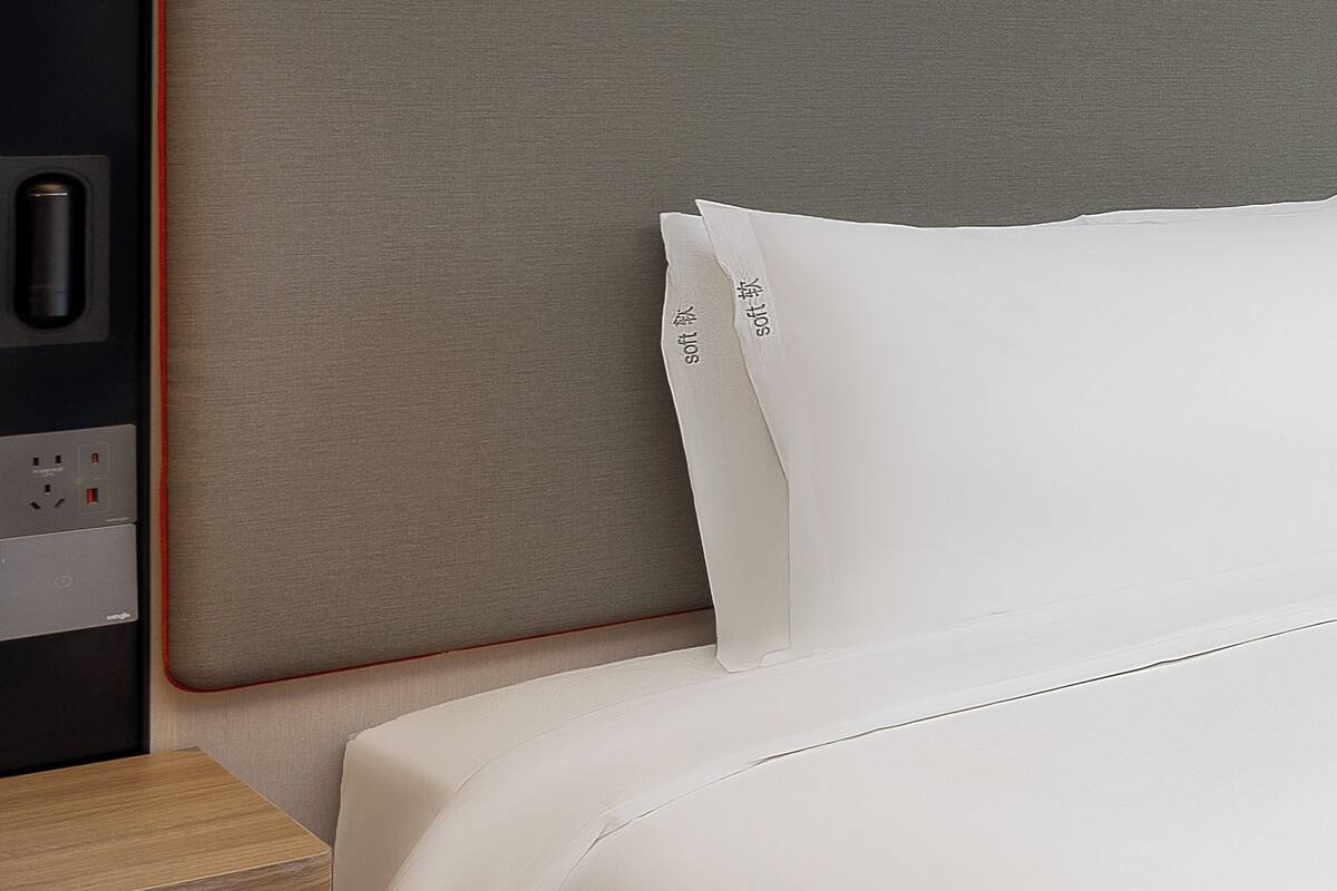 A neatly made bed with white bedding and a headboard with a power outlet.