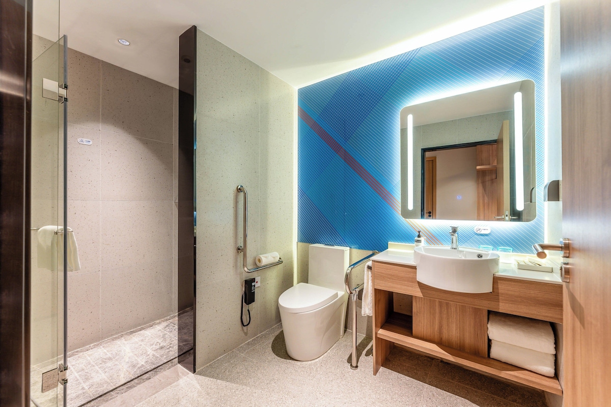 Een moderne badkamer met een douchecabine van glas, een toilet, een wastafel met spiegel en houten opbergkasten.