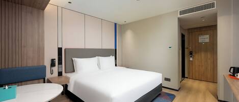A modern hotel room with a large bed, a bedside table, a desk, and a chair.