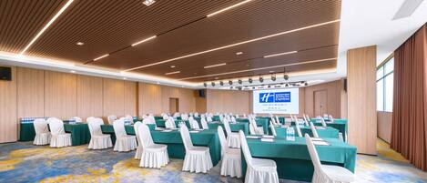 A conference room with rows of tables and chairs, a large screen, and a wooden ceiling.