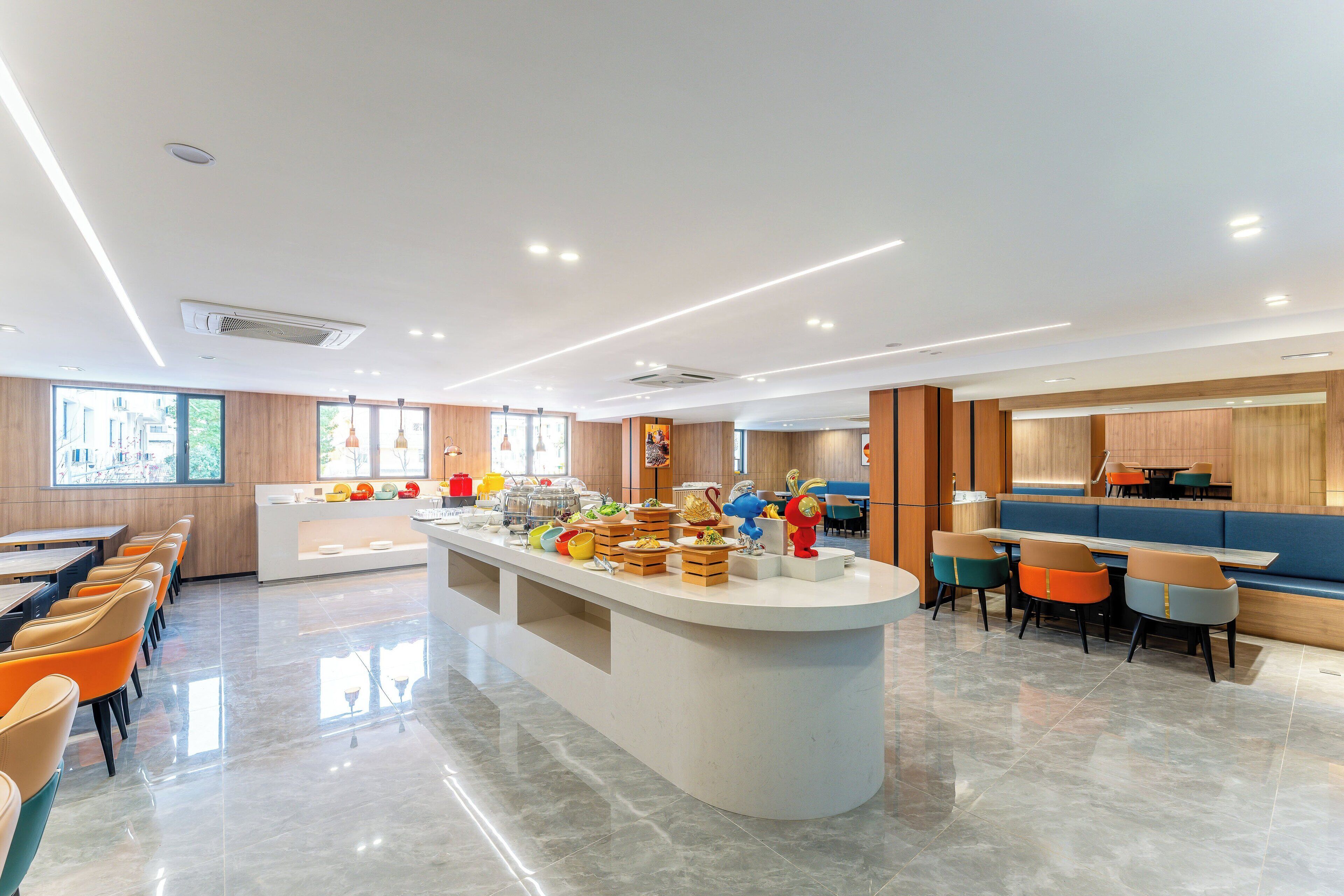 A modern dining area with a central buffet, long communal tables, and a variety of seating options.