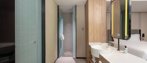 A modern hotel bathroom with two sinks, a large mirror, and a shower area.