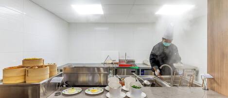 Una cocina con electrodomésticos de acero inoxidable, un mostrador de alimentos y una persona cocinando.