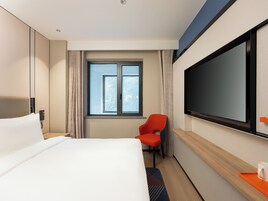 Una habitación de hotel con una cama, una silla roja, un televisor y una ventana con cortinas.
