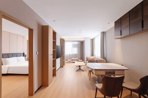 A modern hotel room with a large bed, a desk with chairs, a sofa, and a TV.
