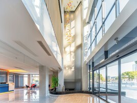A modern hotel lobby with a reception desk, seating area, and large windows offering views of the city.