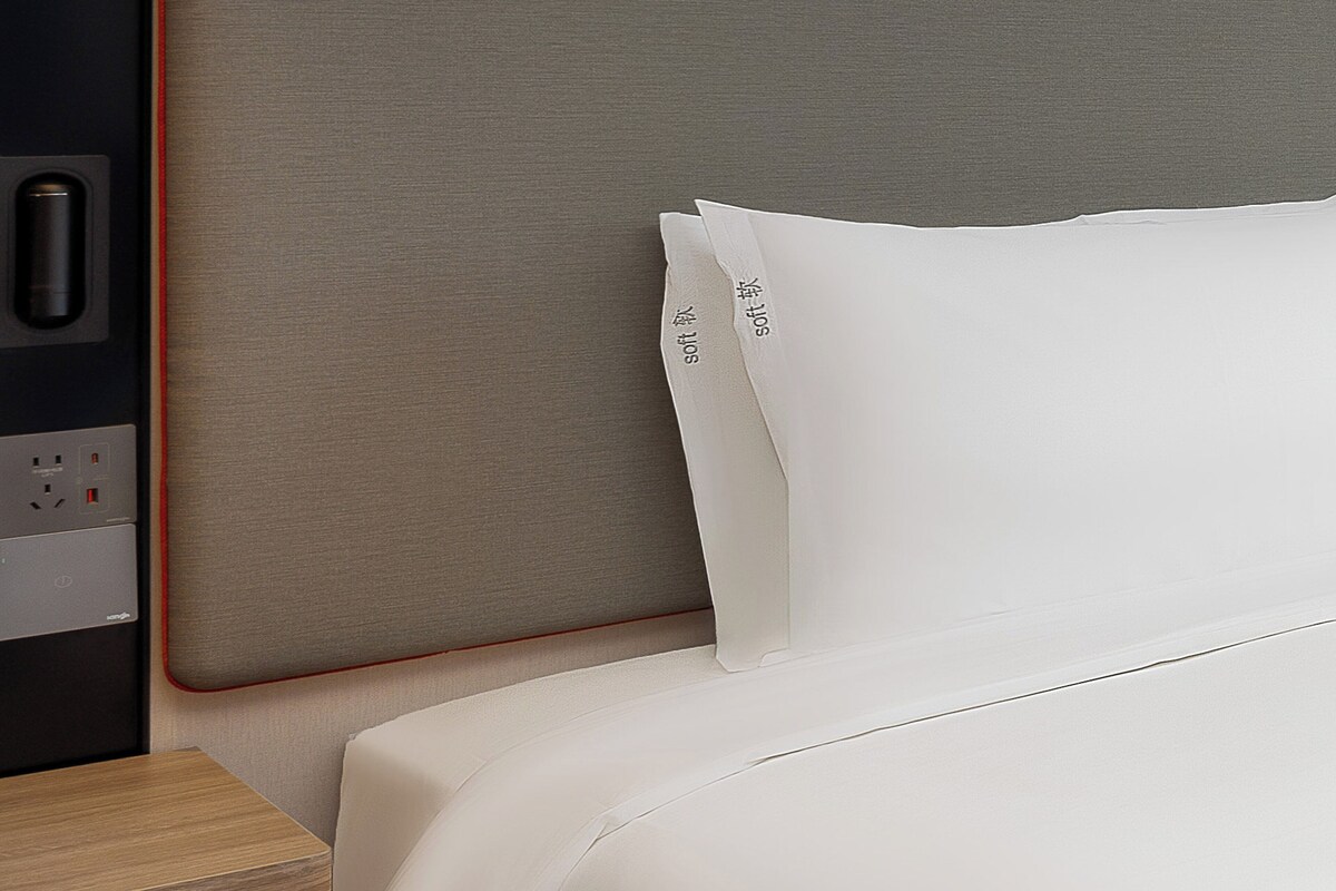 Een net opgemaakt bed met witte lakens en een hoofdbord met een stopcontact.