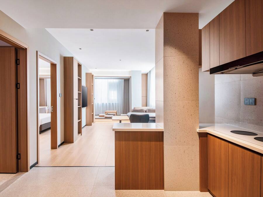 Een moderne hotelkamer met een houten vloer, een groot raam met gordijnen, een flatscreen televisie en een kitchenette met fornuis en magnetron.