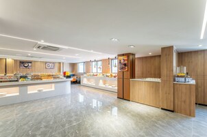 A modern hotel lobby with a central reception desk, a buffet area, and a clean, polished floor.
