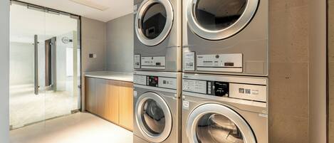 A modern laundry area with stacked front-loading washers and dryers, a glass door leading to a hallway, and a wooden counter.