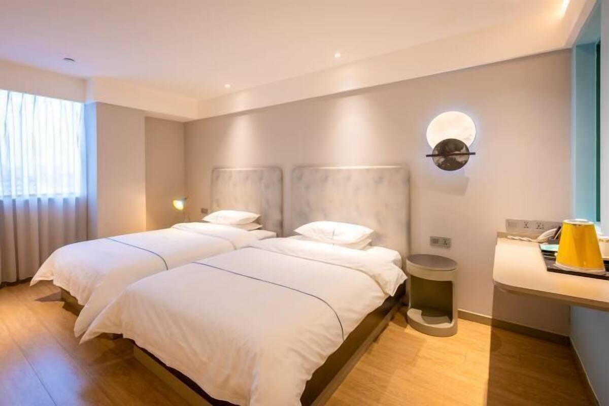 A modern hotel room with two beds, a round wall clock, a small trash bin, and a desk with a telephone.