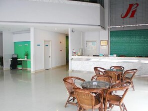 A hotel lobby with a reception desk, wicker chairs, a glass table, and a green wall with a red logo. - Jinjiang Inn (Suzhou baodai ditiezhan dian) (Suzhou)