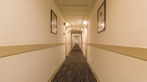 Un pasillo de hotel con pisos alfombrados, cuadros enmarcados en las paredes y un largo corredor que se extiende hasta el final.