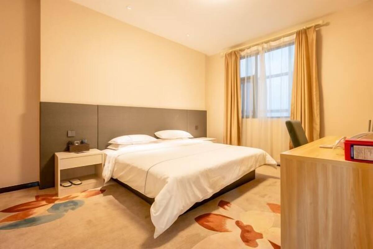 A hotel room with a bed, a nightstand, a desk, and a window with curtains.
