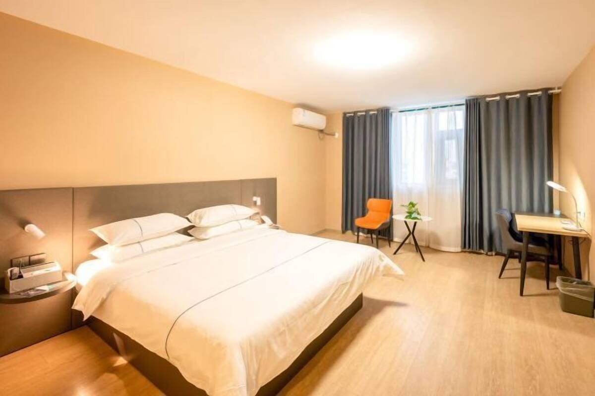A hotel room with a large bed, a desk, a chair, and a small table with a plant.