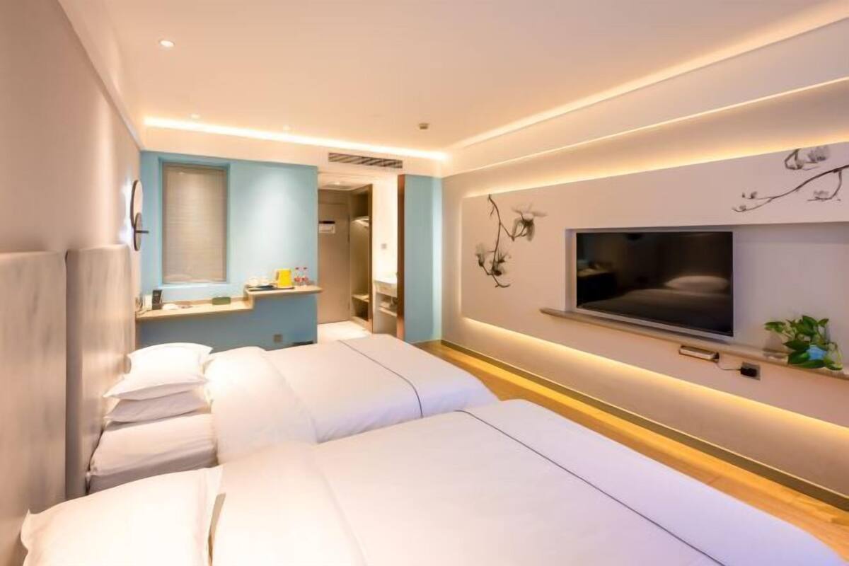 A hotel room with two beds, a TV mounted on the wall, and a small plant on the bedside table.