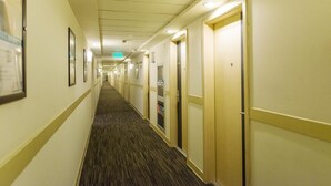 Un pasillo de hotel con pisos alfombrados, puertas a la derecha y cuadros enmarcados a la izquierda.
