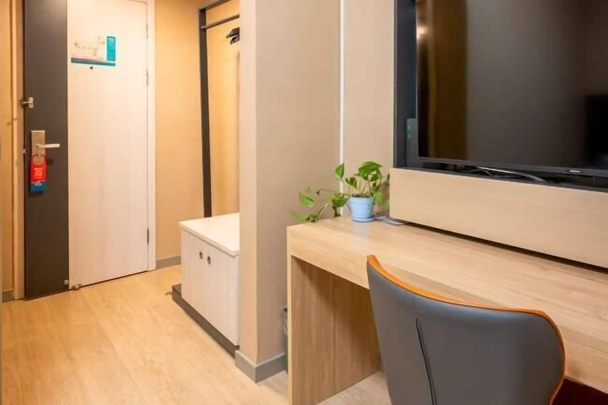 A hotel room with a wooden desk, a chair, a television, and a small plant.
