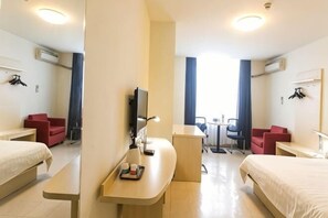 Une chambre d’hôtel avec deux lits, un bureau, une chaise, une télévision et une fenêtre avec des rideaux.