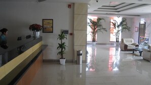 A hotel lobby with a reception desk, potted plants, a seating area with armchairs, and a large window allowing natural light. - Jinjiang Hotel (Suzhou Mudu Zhujiang Road) (Suzhou)