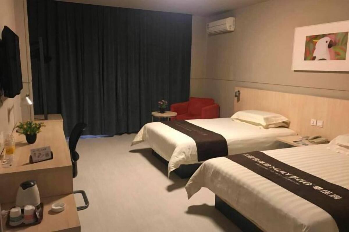 A hotel room with two beds, a desk with a coffee maker, a red chair, and a painting on the wall.