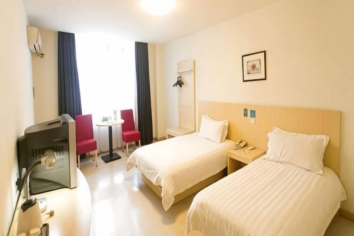 A hotel room with two beds, a desk with a chair, a TV, and a small table.