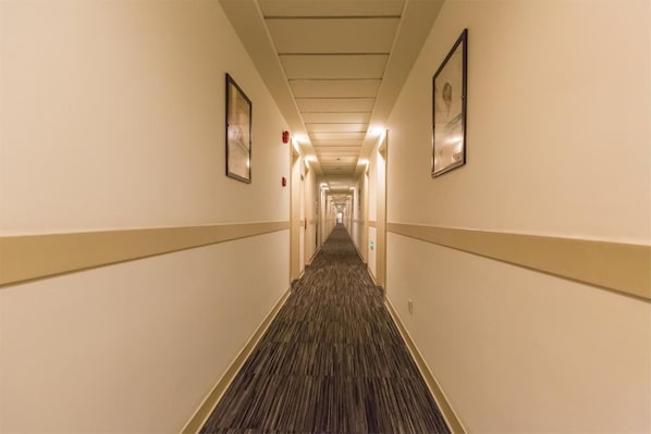 Ein Hotelgang mit Teppichboden, Bildern an den Wänden und einer Decke mit Einbautenleuchten.