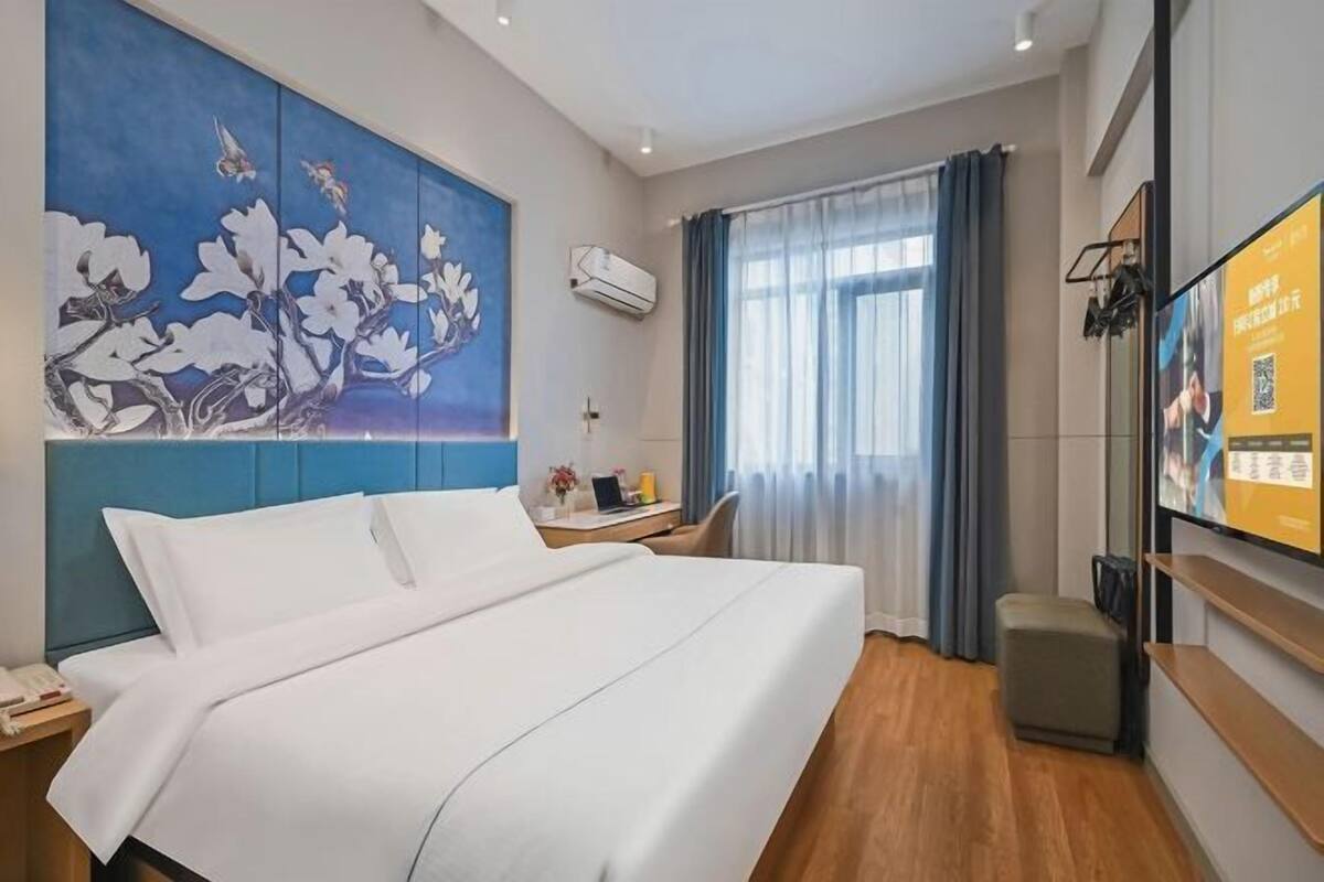 A hotel room with a large bed, a desk with a chair, a TV, and a painting on the wall.