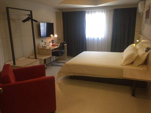 Una habitación de hotel con cama, escritorio, silla, televisor y armario.