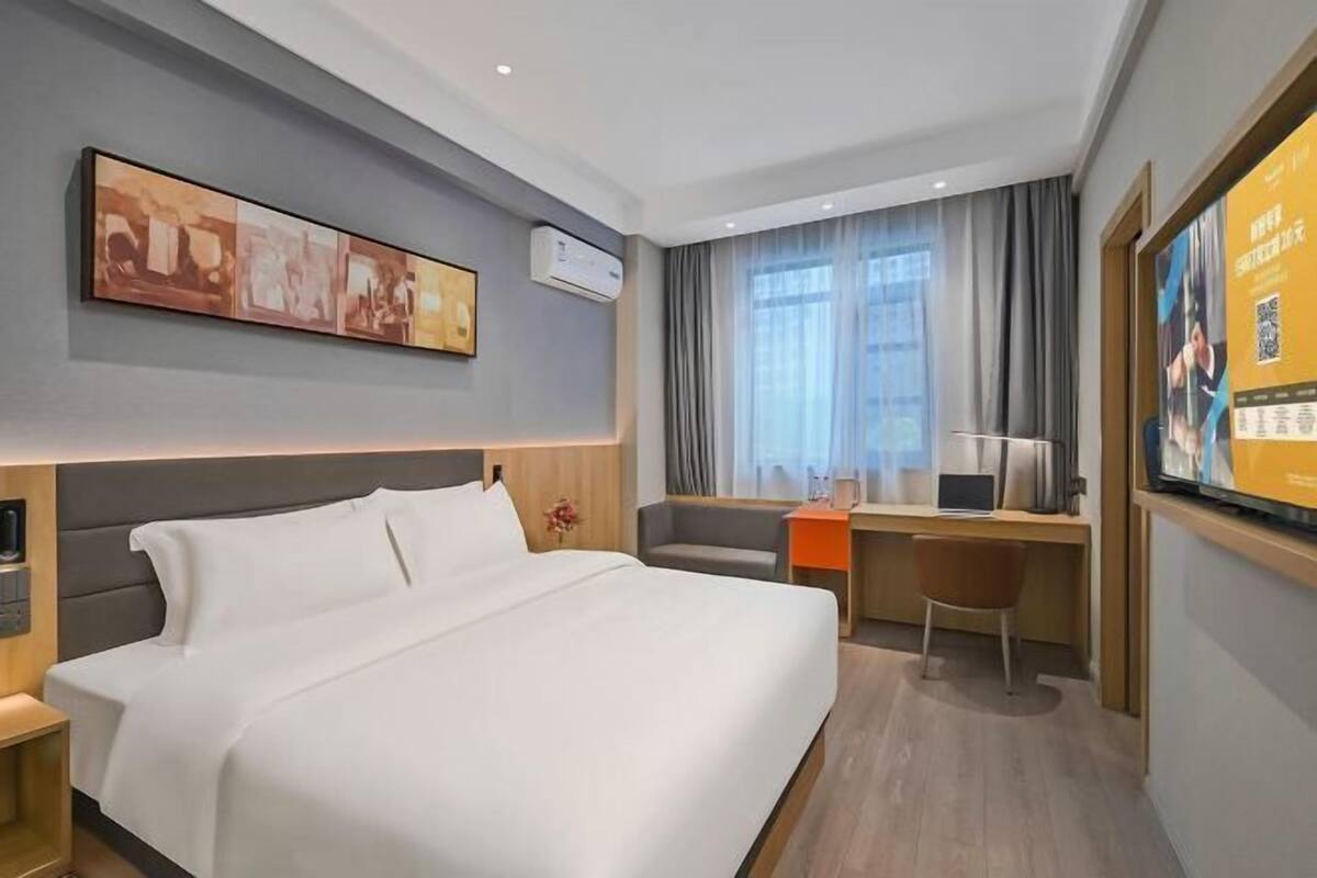 A modern hotel room with a large bed, a desk, a chair, and a television.