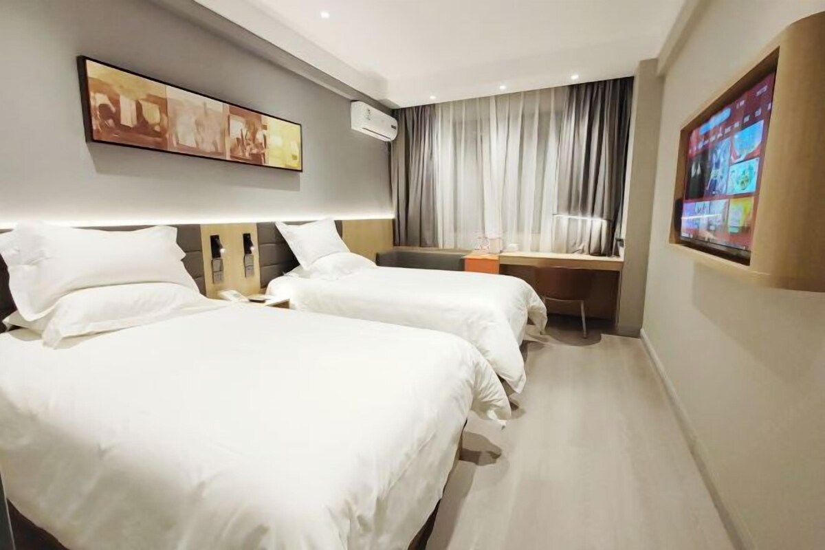 Una habitación de hotel con dos camas, un escritorio, un televisor y un cuadro en la pared.